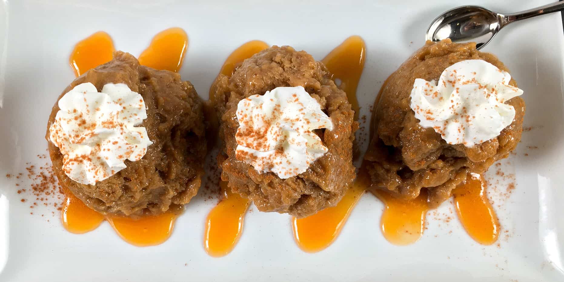 3 pieces of pumpkin spice nice cream with maple syrup topped with whipped cream sprinkled with cinnamon on a rectangular serving white plate with fork