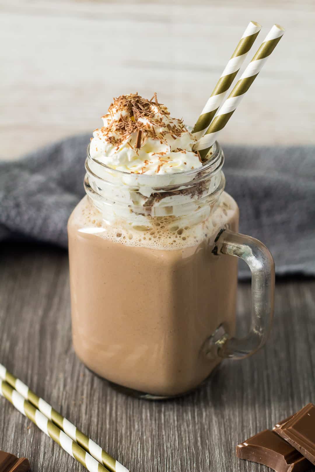 pumpkin spiced hot chocolate with whipped cream and shaved dark chocolates in a glass mug with festive straws