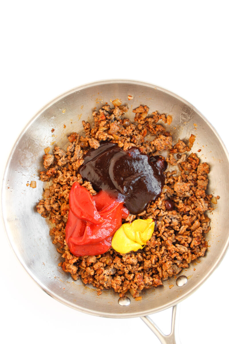 Cooked beef with sauce ingredients in a silver skillet on a white background.