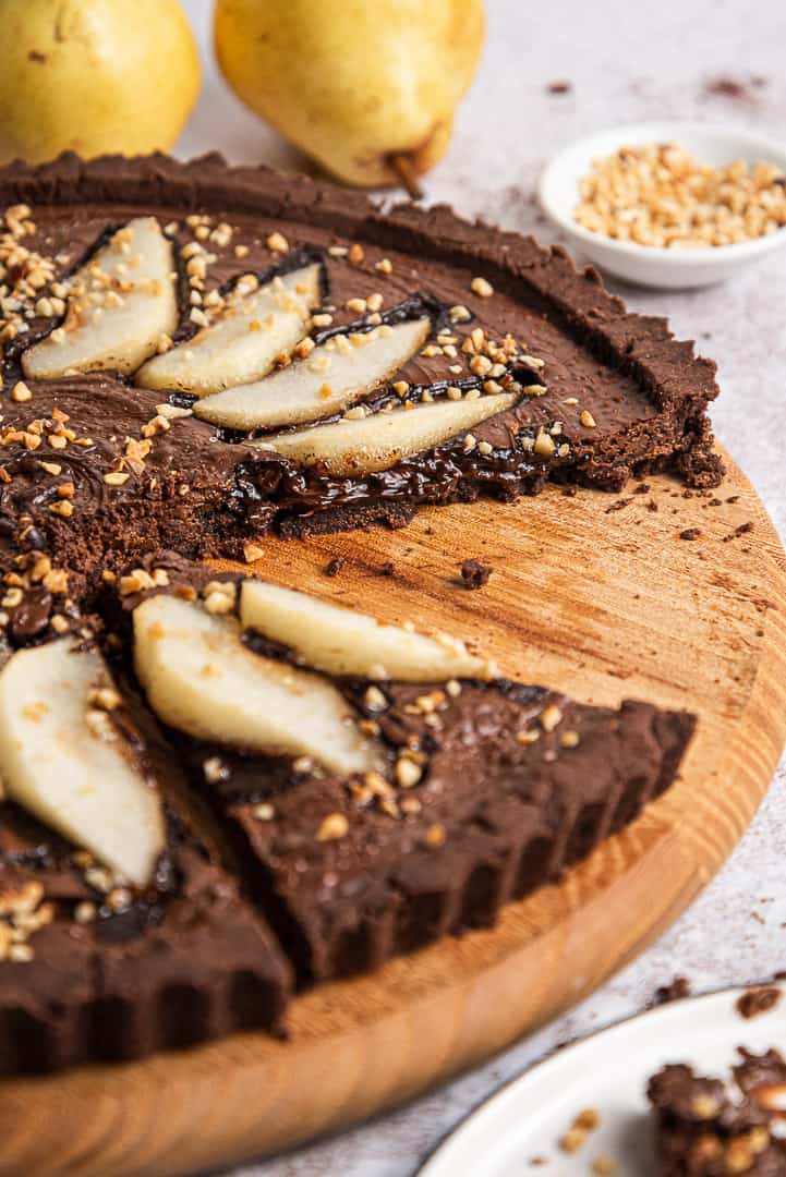 sliced vegan gluten free chocolate tart covered with chocolate spread and rum flavored pears on a wooden circular tray