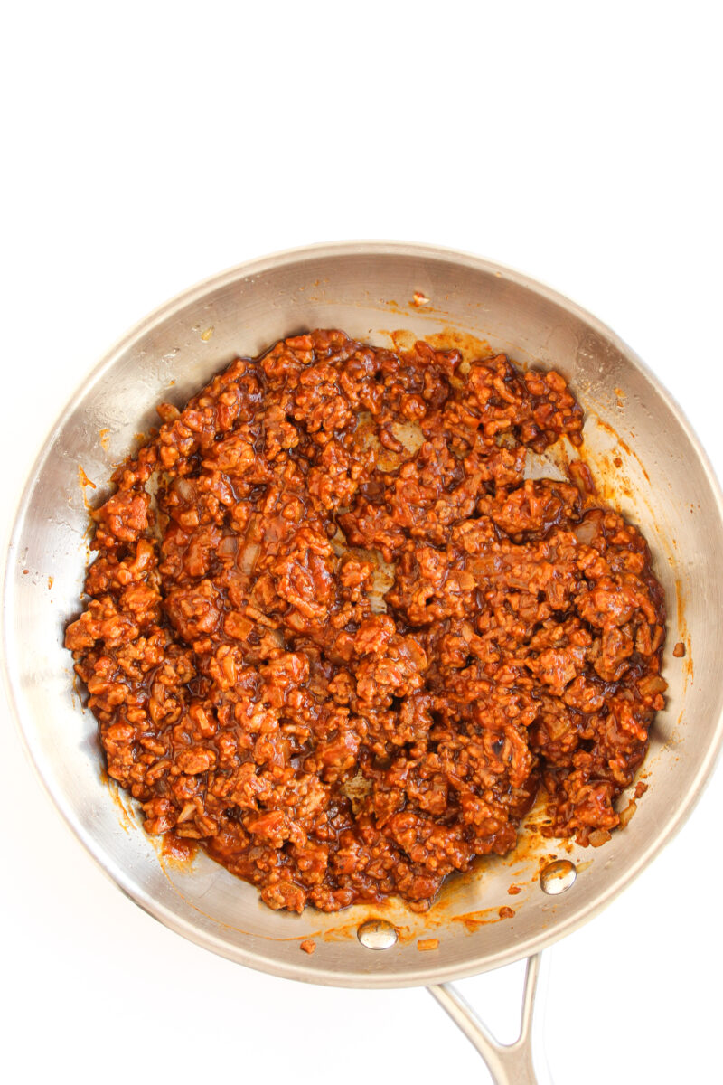 Finished meat mixture in a silver skillet on a white background.