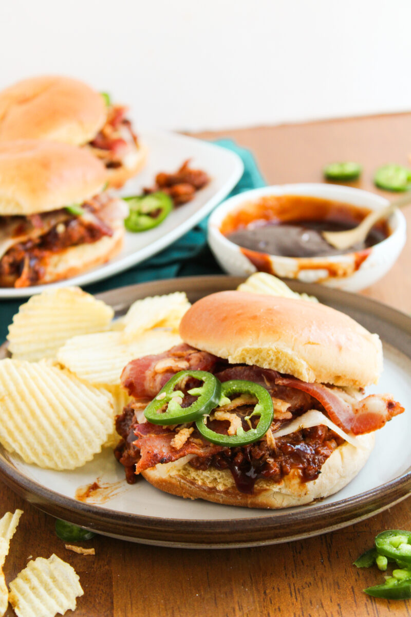 One sloppy joe on a brown plate with chips behind it on a wood background.