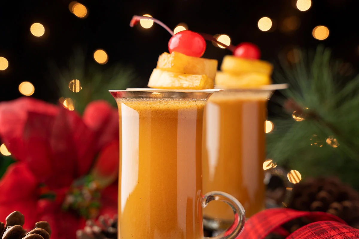 Spiced pineapple hot buttered ram with pineapple slices and cherry on top, festive decorations on the background