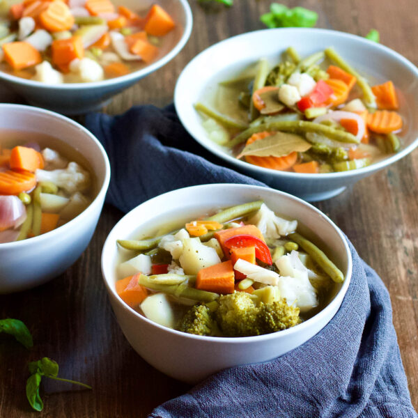 cooked vegetable soup with broccoli, carrots beans and other veggies served in white bowls