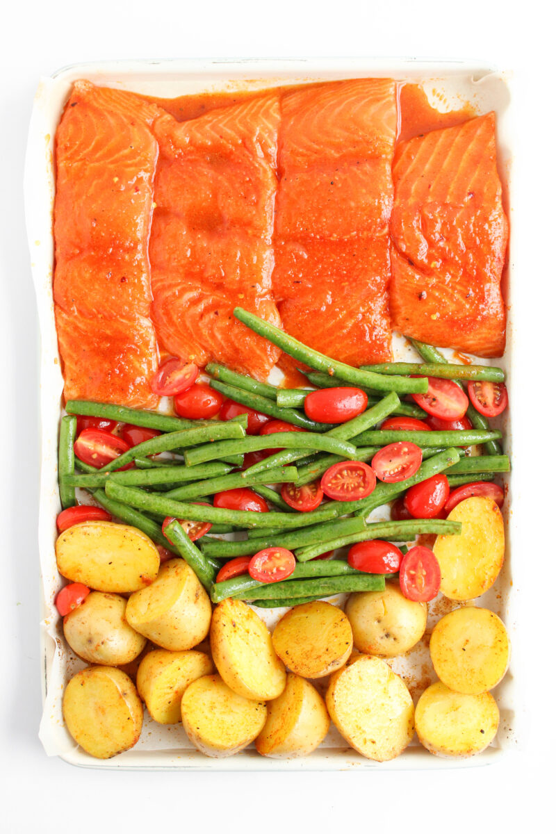 Salmon, vegetables, and potatoes arranged on baking sheet