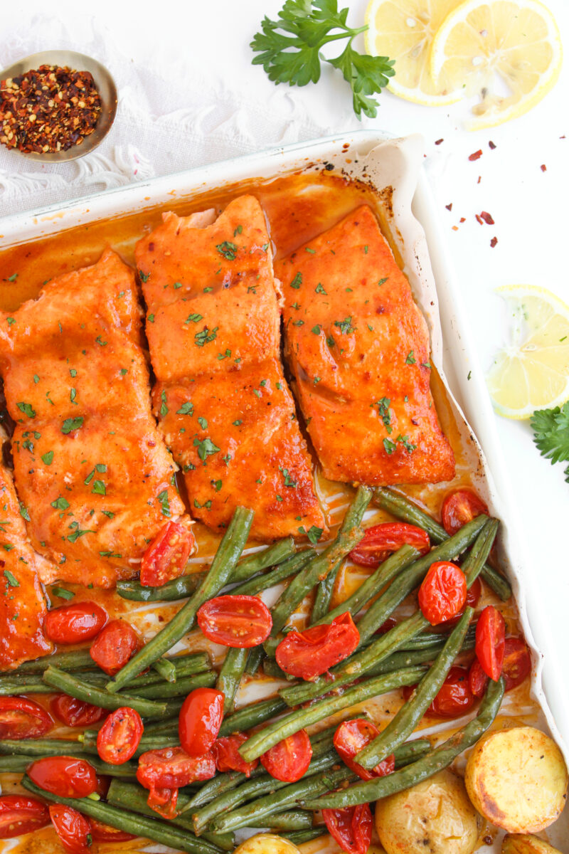 Corner of baking sheet with salmon, vegetables, and potatoes with ingredients scattered around
