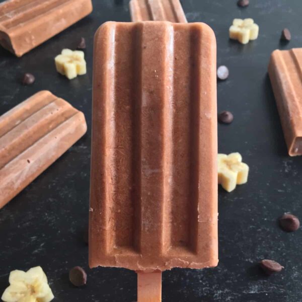 sugar free banana popsicles on a black surface with chocolate chips and flower shape banana cubes 