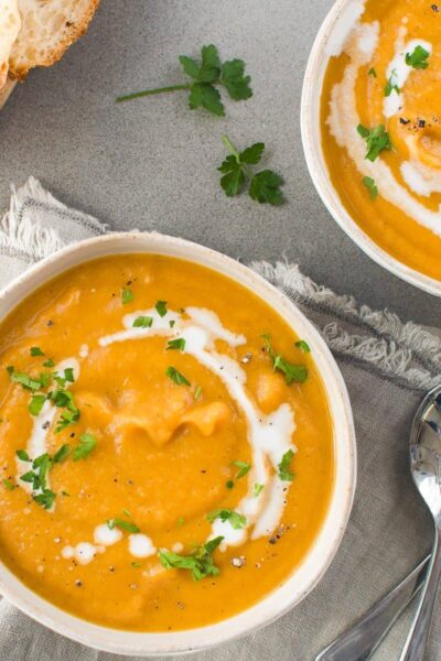 pumpin and sweet potato soup drizzled with cocnut cream and sprinled with herbs in white bowls