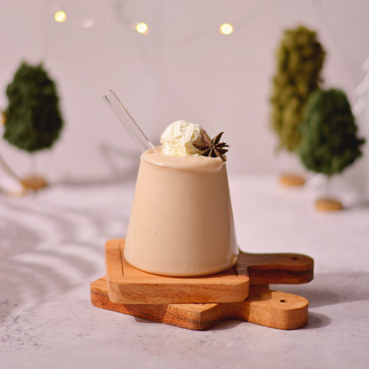 Vegan coquito topped with ice cream and star anise on small stacked wooden tray boards