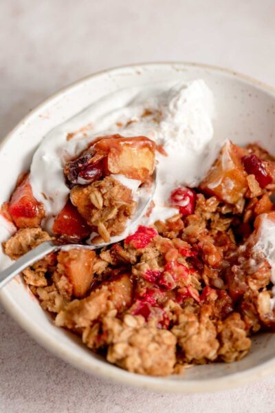 baked apple cranberry oatmeal crisp topped with whipped cream with a spoon on a white bowl