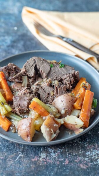 cooked slices of meat with potatoes, carrots and veggies on a blue plate